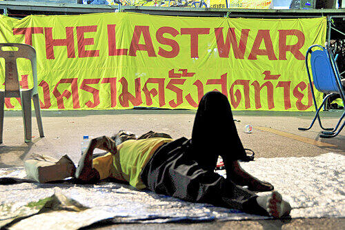 &bdquo;Der letzte Krieg&ldquo;, steht auf dem Plakat. Ein erschöpfter Demonstrant lagert vor dem Regierungssitz in Bangkok.