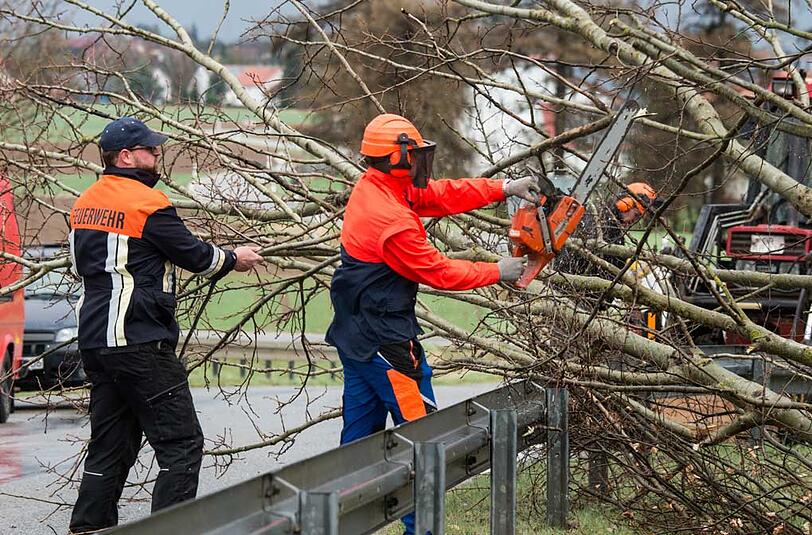 In Oberschneiding (Niederbayern) schaffen Rettungskräfte einen umgestürzten Baum von einer Straße.
