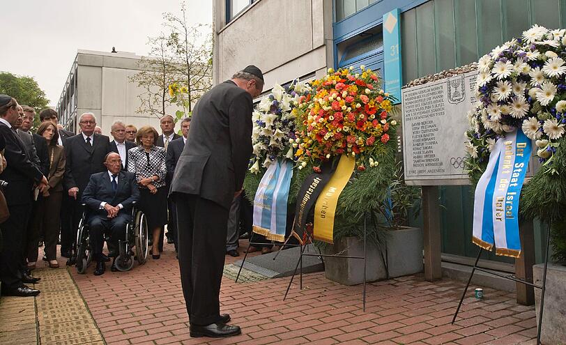 Münchens Oberbürgermeister Christian Ude (SPD, v.r.) verbeugt sich vor der Gedenktafel am ehemaligen Quartier der israelischen Mannschaft von 1972, während im Hintergrund unter anderen der Praesident des Deutschen Olympischen Sportbundes (DOSB), Thomas Bach, Bayerns Kultusminister Ludwig Spaenle (CSU), Charlotte Knobloch, und das israelische Mitglied des Internationalen Olympischen Komitees (IOC), Alex Gilady (im Rollstuhl) sind.