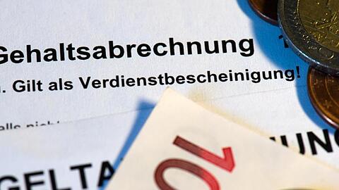 Auf einer Gehaltsabrechnung liegen Euro-Münzen. Foto: Arno Burgi/dpa-Zentralbild/dpa/Illustration