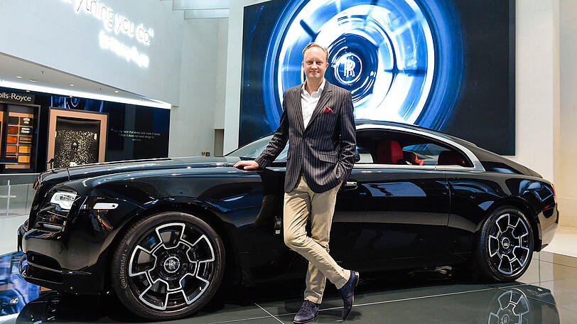 Ein Auto, so britisch wie sein Designer: Giles Taylor lehnt in der BMW Welt lässig an einem Rolls-Royce Wraith in der Sonderedition Black Badge. Das Auto hat einen Grundpreis von 339.804 Euro. Der Motor leistet 612 PS, was dem 2,5 Tonnen schweren und über fünf Meter langen Gefährt eine Höchstgeschwindigkeit von 250 km/h ermöglicht.