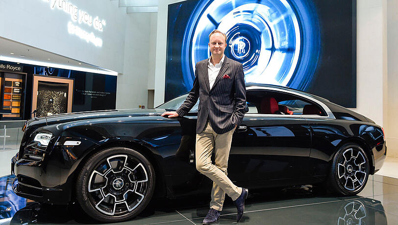 Ein Auto, so britisch wie sein Designer: Giles Taylor lehnt in der BMW Welt lässig an einem Rolls-Royce Wraith in der Sonderedition Black Badge. Das Auto hat einen Grundpreis von 339.804 Euro. Der Motor leistet 612 PS, was dem 2,5 Tonnen schweren und über fünf Meter langen Gefährt eine Höchstgeschwindigkeit von 250 km/h ermöglicht.