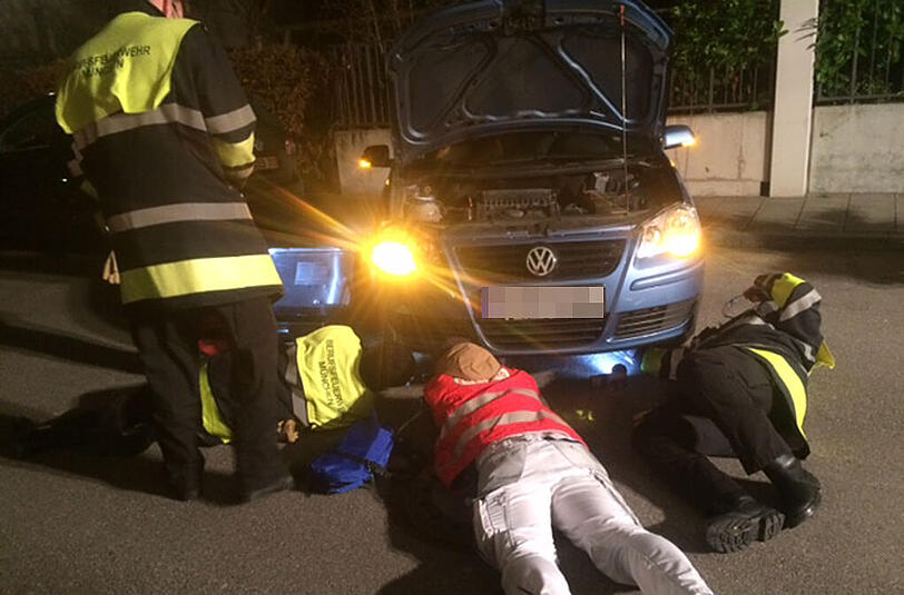Helfer der Tierrettung München versuchen, eine Katze aus dem Motorraum eines Autos zu befreien.