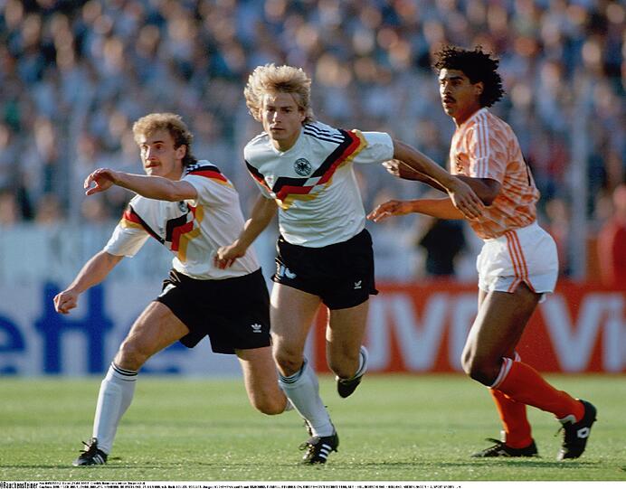 21. Juni 1988, EM-Halbfinale in Hamburg, DFB-Niederlande 1:2 (0:0)
Das Hass-Spiel. `Wir fressen sie auf!", brüllt Oranje-Kapitän Ruud Gullit vorher, Abwehrchef Ronald Koeman ist im Siegesrausch derart aufgeladen, dass er sich mit Thons Trikot den Allerwertesten abwischt, auf der Tribüne zeigt ein Radioreporter den deutschen Kollegen sein entblößtes Hinterteil. &bdquo;Lothar, Lother, alles ist vorbei&ldquo;, singt die Elftal in der Kabine, als Franz Beckenbauer zum Gratulieren kommt. Michels, mittlerweile wieder im Amt, bekommt endlich seinen Sieg, in der Heimat kommt es zur größten Massenkundgebung seit der Befreiung von den Nazis 1945. De Telegraaf titelt: `Endlich Rache!" Und der Poet Jules Deelder schreibt: &bdquo;Sie, die fielen, erhoben sich jauchzend aus ihrem Grab.&ldquo;