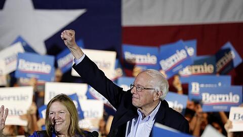 Bernie Sanders und seine Frau Jane stehen bei einer Wahlkampfveranstaltung inmitten von Anhängern.