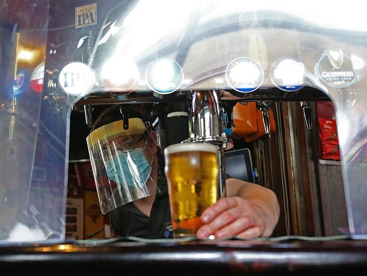 Ein Barkeeper im Pub zapft ein Glas Bier mit Mundschutz und Visier vor der Wiedereröffnung.