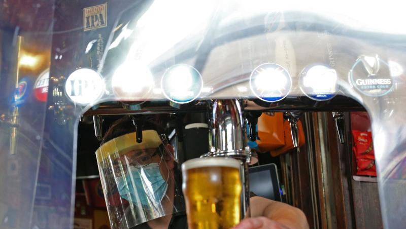 Ein Barkeeper im Pub zapft ein Glas Bier mit Mundschutz und Visier vor der Wiedereröffnung. Ein Barkeeper im Pub zapft ein Glas Bier mit Mundschutz und Visier vor der Wiedereröffnung.