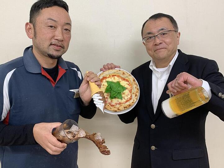 Fabrikleiter Hiroaki Miyazawa (l.) und Firmensprecher Yuta Kurokawa mit Repliken: eine Pizza, eine Maß Bier, eine Cola mit Eiswürfeln während des Einschüttens und ein Softeis.