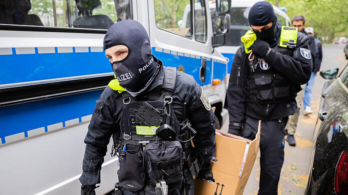 Polizisten tragen bei einer Hausdurchsuchung in Berlin-Kreuzberg einen Karton zu einem Fahrzeug. Dem zugrunde liegen Ermittlungen aus München.