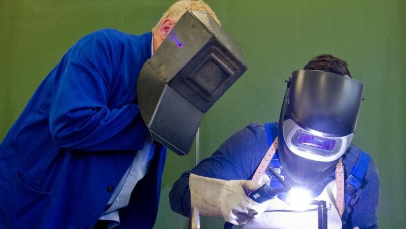 Ein Auszubildender (r) setzt eine Schweißnaht an ein Metallteil. Ein Auszubildender (r) setzt eine Schweißnaht an ein Metallteil.