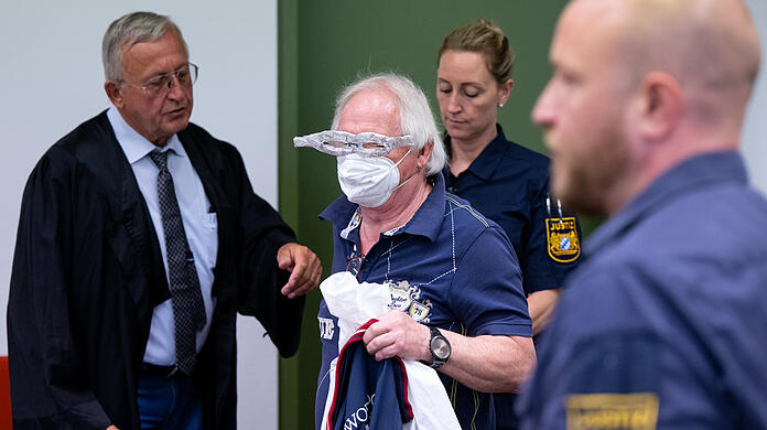 Der Angeklagte (mit Alubrille) im Prozess um gefälschte Impfpässe steht vor Beginn der Verhandlung zusammen mit seinem Anwalt Franz Wittl (l.) im Gerichtssaal.