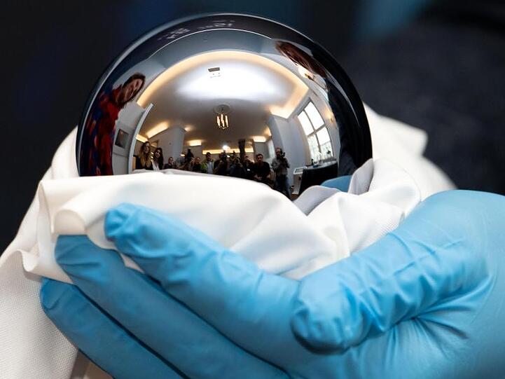 Ein Mann hält eine exakt ein Kilogramm schwere, hochreine Siliziumkugel in den Händen. Foto: Sven Hoppe