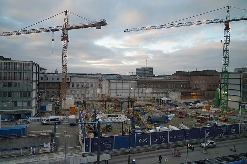 Bagger, Lastwagen, Kräne, Kieshaufen und jede Menge Eisen: Große Teile der Baustelle am Vorplatz des Münchner Hauptbahnhofs sind aktuell hinter dem blauen Bauzaun versteckt. Noch bis 2030 wird hier herumgerissen und neu gebaut, bis der neue Bahnhof fertig sein soll.