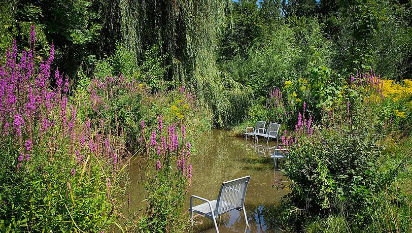 Im Rosengarten in Untergiesing fließt ein Bacherl, zwischen Bäumen und bunten Sträuchern hindurch.  Auf den Stühlen lässt es sich wunderbar entspannen.