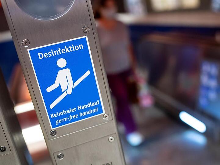 Ein Schild mit der Aufschrift "Desinfektion - Keimfreier Handlauf" ist an einer Rolltreppe zu sehen. Foto: Sven Hoppe/dpa