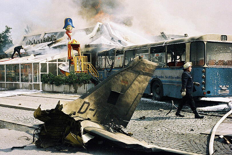 Der Absturz: Ein zerstörter Bus, eine brennende McDonalds-Filiale und das Trümmerteil eines Flugzeugs: Hier ist eine der schlimmsten Flugzeugkatastrophen zu sehen, die München je erlebt hat.
Am 11. August 1987 gerät eine zweimotorige Piper Cheyenne bei einem Prüfungsflug über Trudering außer Kontrolle und stürzt auf den Bus und das Restaurant. Ein Großbrand bricht aus. Erst nach einer Stunde können die Einheiten der Münchner Feuerwehr die Flammen mit 22 Rohren und Werfern unter Kontrolle bringen. Neun Menschen sterben.