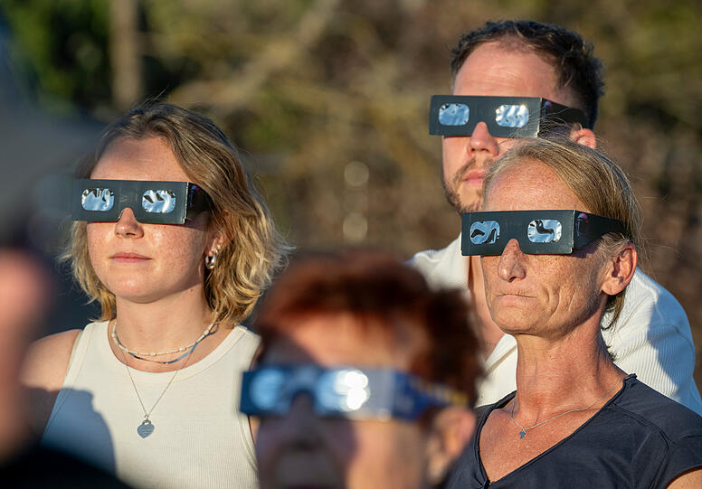 Besucher auf der Dachterrasse des Kulturzentrums Gasteig schauen mit speziellen Brillen auf die Sonnenfinsternis.