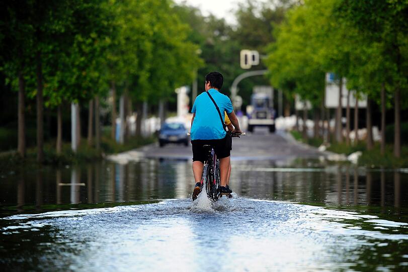 Ein Junge fährt mit seinem Fahrrad in Magdeburg durch eine überflutete Straße.