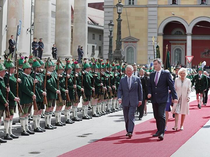 Der britische Thronfolger Prinz Charles (l) und seine Frau Camilla (r) werden von dem bayerischen Ministerpräsidenten Markus Söder (CSU, M), vor der historischen Residenz auf dem Max-Joseph-Platz empfangen. Foto: Steve Parsons/PA Wire