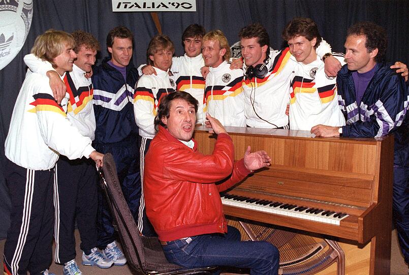 1989 tat er es gleich wieder:  "Sempre Roma" lautete der Titel in Vorbereitung auf die Fußball-WM 1990 in Italien. Um den sitzenden Udo Jürgens am Klavier hatten sich versammelt (v.l.): Jürgen Klinsmann, Rudi Völler, Asistenztrainer Holger Osieck, Frank Mill, Thomas Berthold, Andreas Brehme, Lothar Matthäus, Andreas Möller und Trainer Franz Beckenbauer.