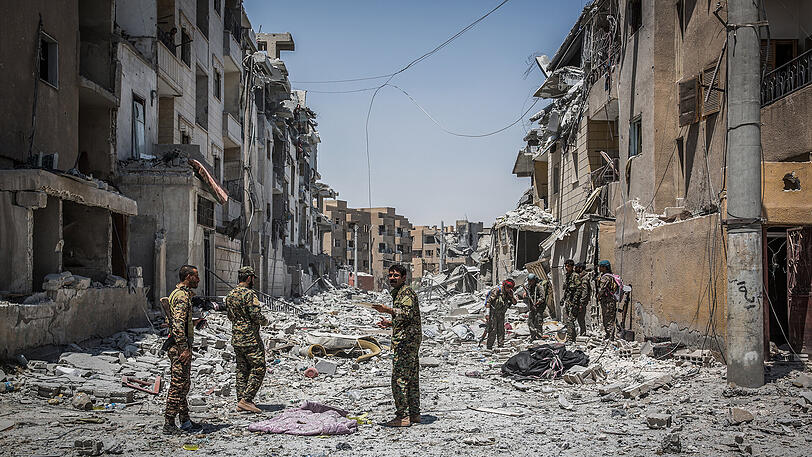Soldaten der Syrischen Demokratischen Kräfte gehen in Al-Rakka durch einen zerstörten Straßenzug.