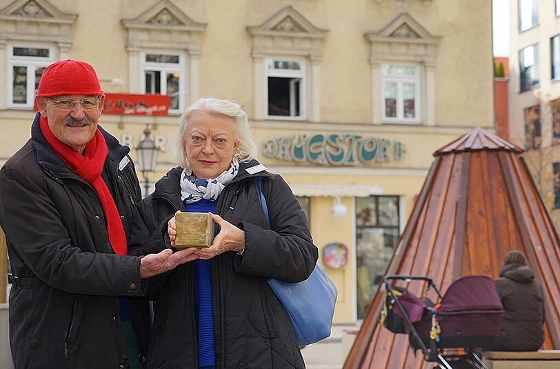 Klaus und Janne Weinzierl am Wedekindplatz. Sie halten einen Stolperstein in den Händen.