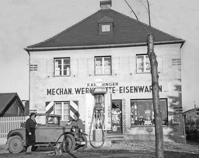 Diese Fotografie ist vom gleichen Standort aufgenommen. Es zeigt unser 1931 erbautes Haus ungefähr im Jahre 1936 auf eben jenem Grundstück! Es war bis in die 50er Jahre hinein eine Auto- und Motorradwerkstatt mit Tankstelle. Danach war darin ein Fahrradgeschäft. Heute beherbergt es uns und einen Kinderschuhladen.
Die Dame auf dem alten Foto ist Oma Kröninger, die Großmutter meines Adoptivvaters Helmut Biber.
