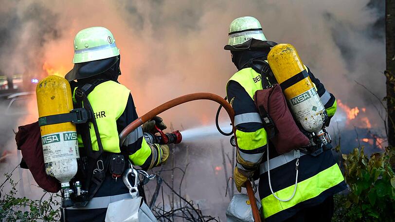 Feuerwehrkräfte mit schwerem Atemschutz löschen den Wohnwagen unter der Eisenbahnbrücke in Untergiesing.