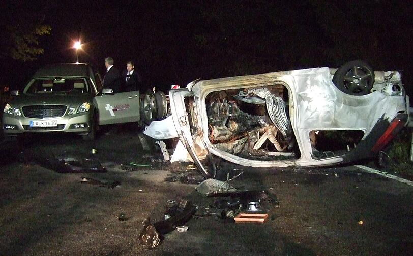 Bestatter stehen in der Nacht auf Donnerstag (18.08.2011) bei Thyrnau neben einem ausgebrannten Auto.