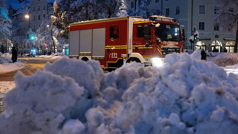 Ein Feuerwehrauto fährt hinter einem zusammengeräumten Schneehaufen entlang.