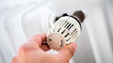 Ein Mann dreht in einer Wohnung am Thermostat einer Heizung.