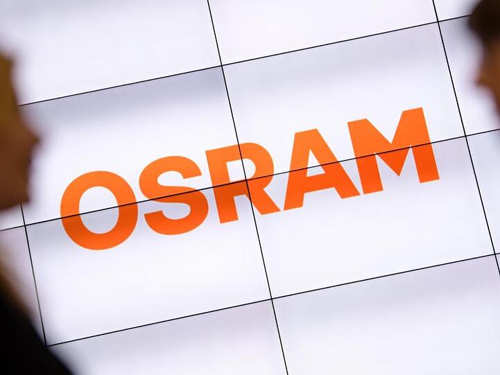 Zwei Silhouetten stehen neben dem Firmenlogo von Osram. Foto: Matthias Balk/Archivbild