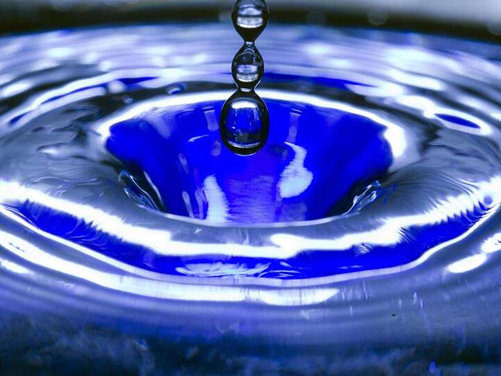 Ein Wassertropfen fällt in eine blaue Wasserschüssel. Foto: Jens Büttner/zb/dpa/Archivbild