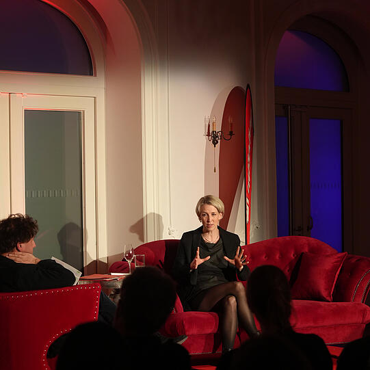 Adrian Prechtel im Gespräch mit Bürgermeisterin Katrin Habenschaden auf dem roten Sofa (von Möbel Höffner) in München.