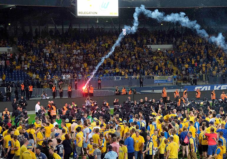 Braunschweiger Fans stehen Polizisten und Ordnern nach dem Abpfiff auf dem Platz gegenüber.
