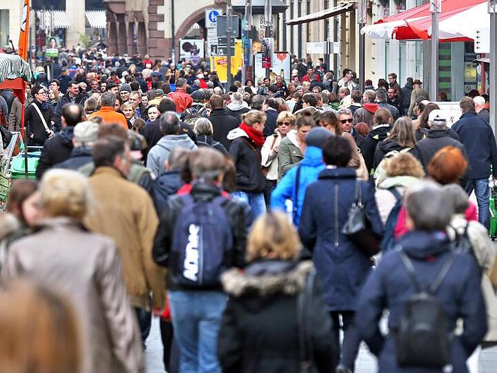 Passanten flanieren durch eine Fußgängerzone.