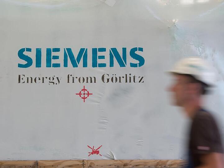 Ein Siemens-Mitarbeiter mit Schutzhelm geht an einer Folie mit dem Aufdruck "Siemens Energy from Görlitz" vorbei. Foto: Sebastian Kahnert/zb/dpa/Archivbild