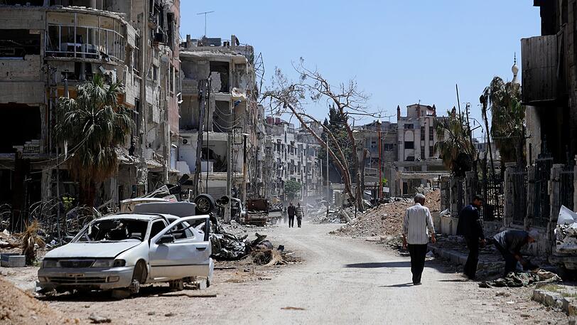 Menschen gehen an zerstörten Häusern und Autos im Vorort der syrischen Hauptstadt Damaskus vorbei. Der Westen macht die syrische Regierung für den mutmaßlichen Einsatz von Chemiewaffen in der ehemaligen Rebellenhochburg Duma verantwortlich.