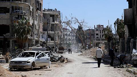 Menschen gehen an zerstörten Häusern und Autos im Vorort der syrischen Hauptstadt Damaskus vorbei. Der Westen macht die syrische Regierung für den mutmaßlichen Einsatz von Chemiewaffen in der ehemaligen Rebellenhochburg Duma verantwortlich.
