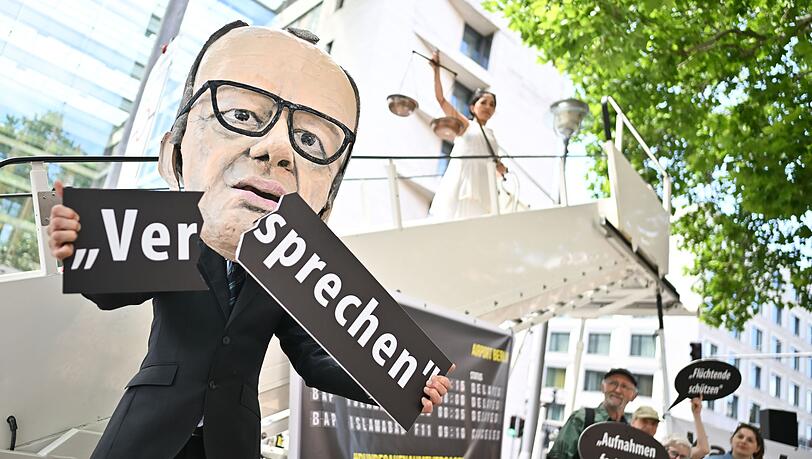 Ein Aktivist mit Merz-Maske zerbricht während einer symbolischen Protestaktion von Kabul Luftbrücke und Campact ein Schild mit der Aufschrift "Versprechen".