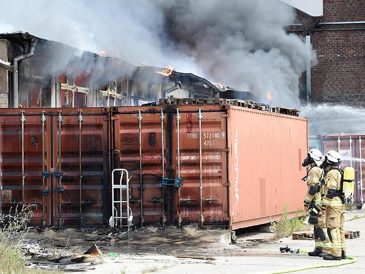 Feuerwehrleute stehen vor einem vom Brand beschädigten Container.