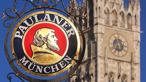 Logo der Brauerei Paulaner an einer Gastst&auml;tte mit Turm des Rathaus es in der Innenstadt M&uuml;nchen