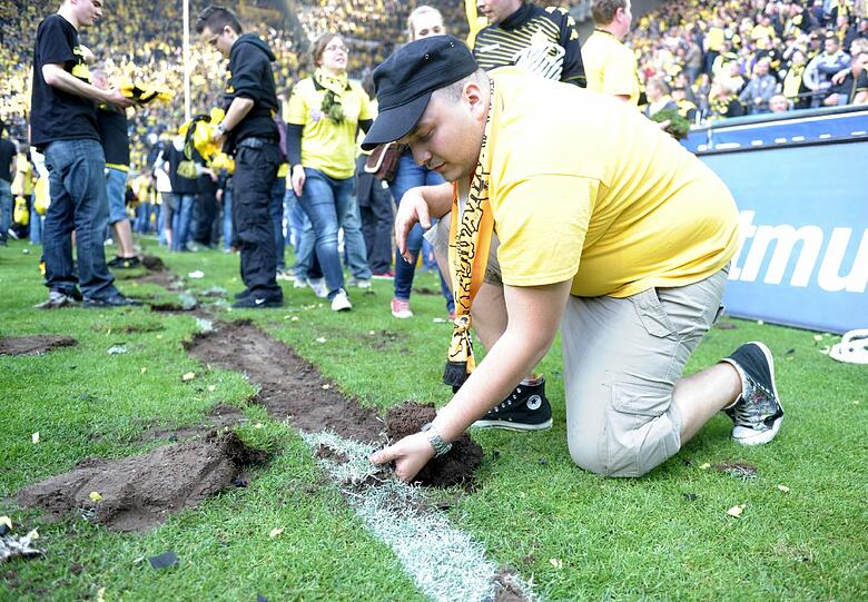 Die Fans wollen den Triumph bewahren. Sie nehmen sich ein Stückchen Rasen aus dem Stadion mit nach Hause.