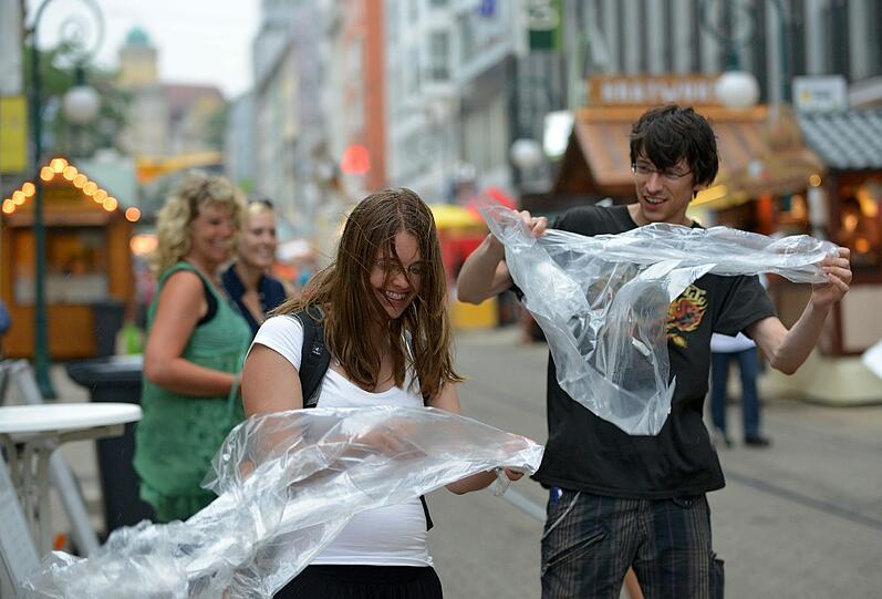 Hessentagsbesucher mühen sich am 20.06.2013 in Kassel (Hessen) im Gewitterregen ab, einen Plastik-Regenschutz anzulegen. Ein Gewitter zog am Nachmittag über die Stadt und vertrieb die größte Hitze.