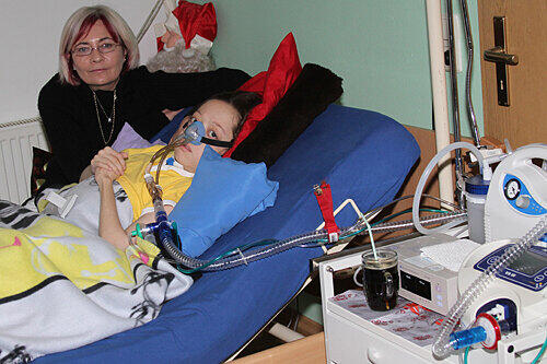 Petra L. sitzt am Krankenbett ihres Sohnes Kevin, der beatmet werden muss. Das Bett kann er nur mit Hilfe von Pflegern verlassen.