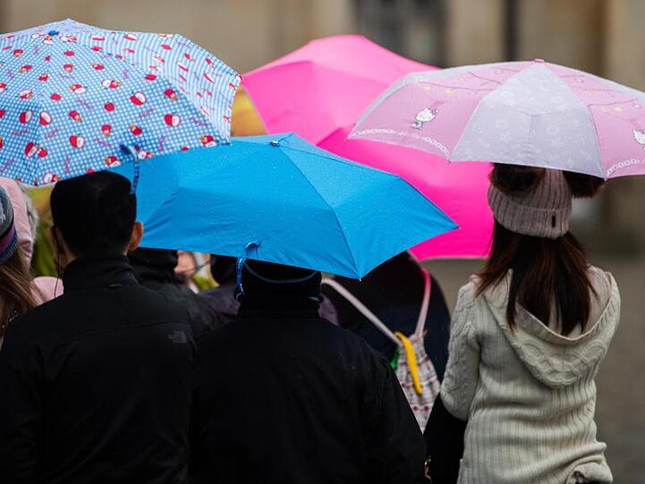 Menschen gehen mit Regenschirmen durch die Innenstadt. Foto: Robert Michael/dpa-Zentralbild/dpa/Symbolbild
