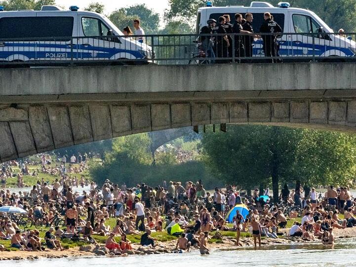 Hunderte Menschen sonnen sich neben der Isar, auf der Brücke stehen Polizisten. Foto: Peter Kneffel/dpa/Archivbild