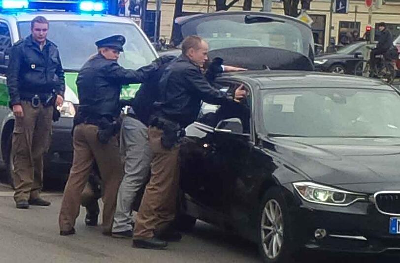 Die Polizei drückt einen der Tatverdächtigen gegen das Einsatzfahrzeug...