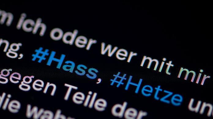 Auf dem Bildschirm eines Smartphones sieht man die Hashtags Hass und Hetze.