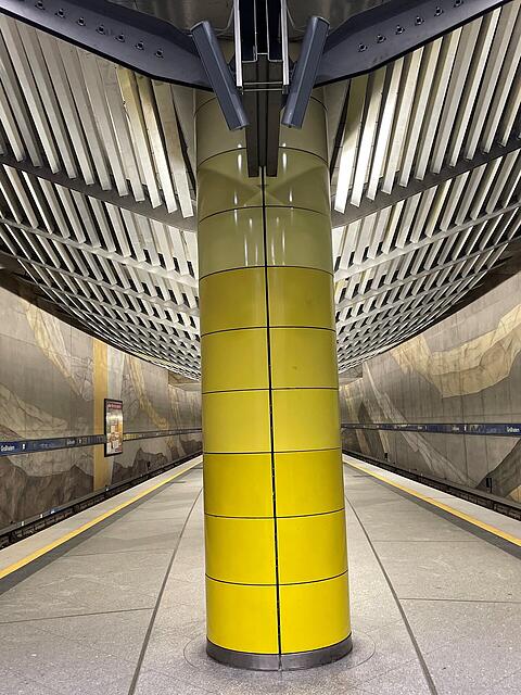 Der U-Bahnhof Gro&szlig;hadern mit gelber S&auml;ule, Wandgem&auml;lde und moderner Lichtabdeckung.